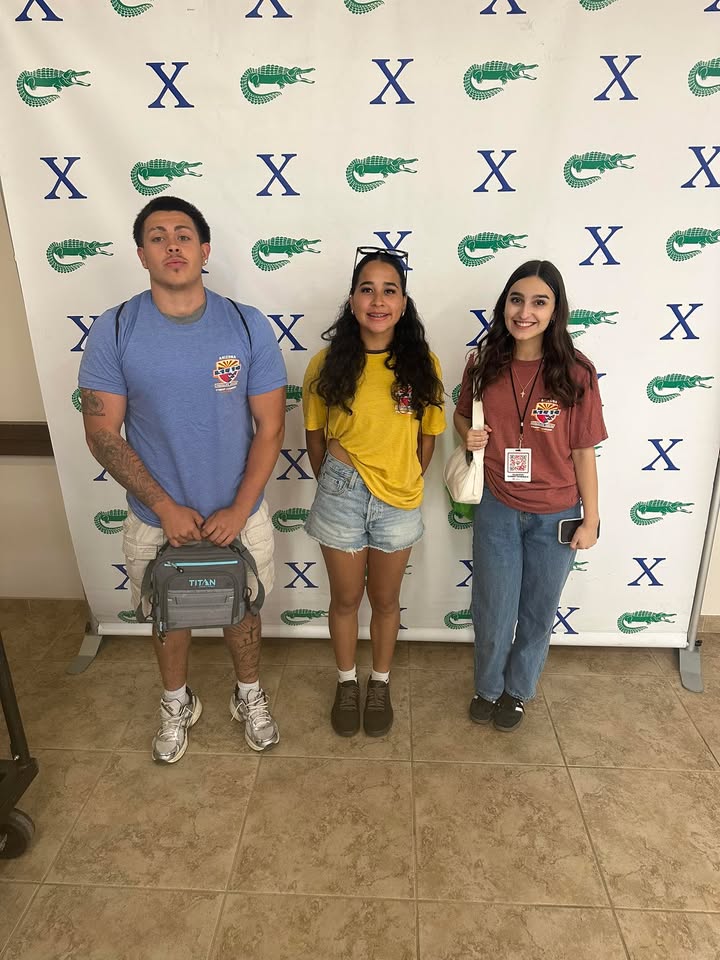 Three students stand in front of a backdrop