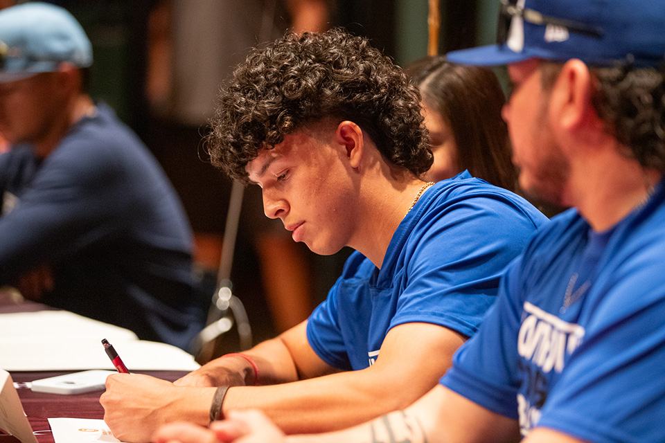 A teen boy in a blue t-shirt signs his letter of intent
