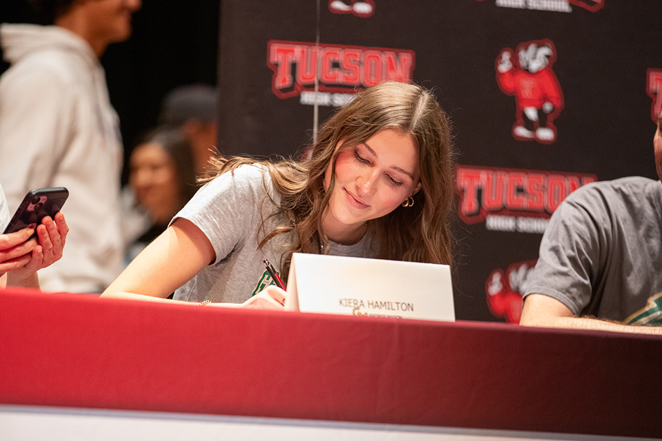 A teen girl in a gray t-shirt signs her letter of intent